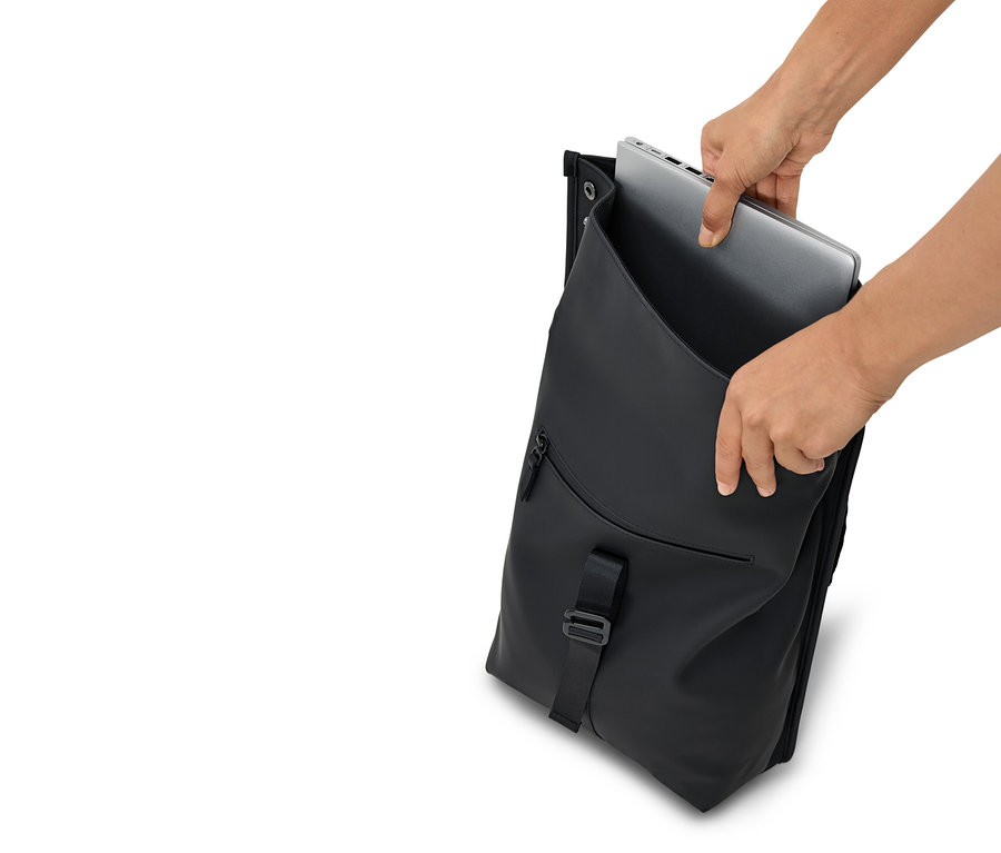 Eller açık siyah bir sırt çantasına gümüş bir dizüstü bilgisayar yerleştiriyor.