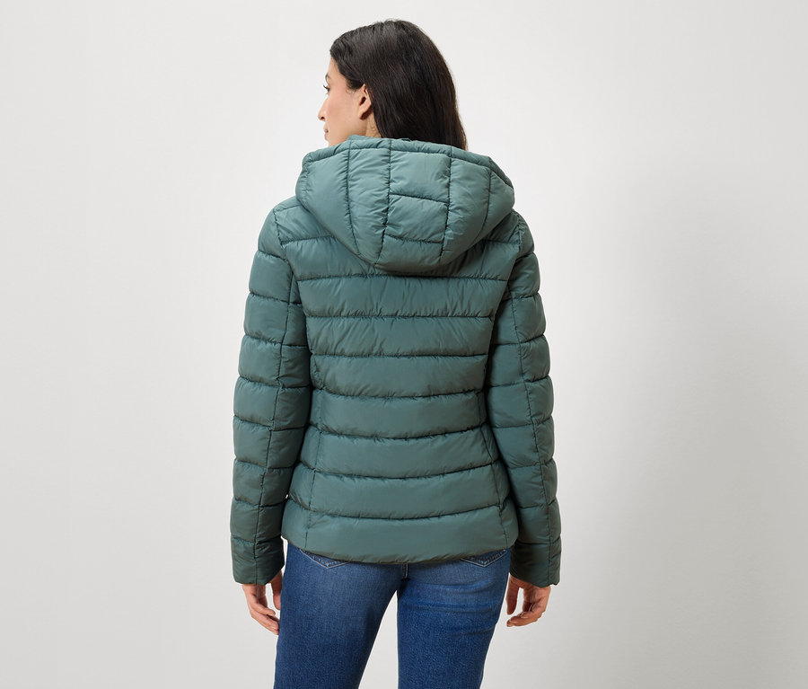 Sırtı kameraya dönük bir kadın, yeşil bir şişme mont ve kot pantolon giyiyor.