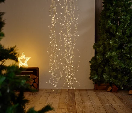 Yıldız şeklinde ışıklı bir dekorasyon, aşağı doğru sarkan ışık zincirleriyle asılı duruyor, yanında bir Noel ağacı ve parlayan bir yıldız var.