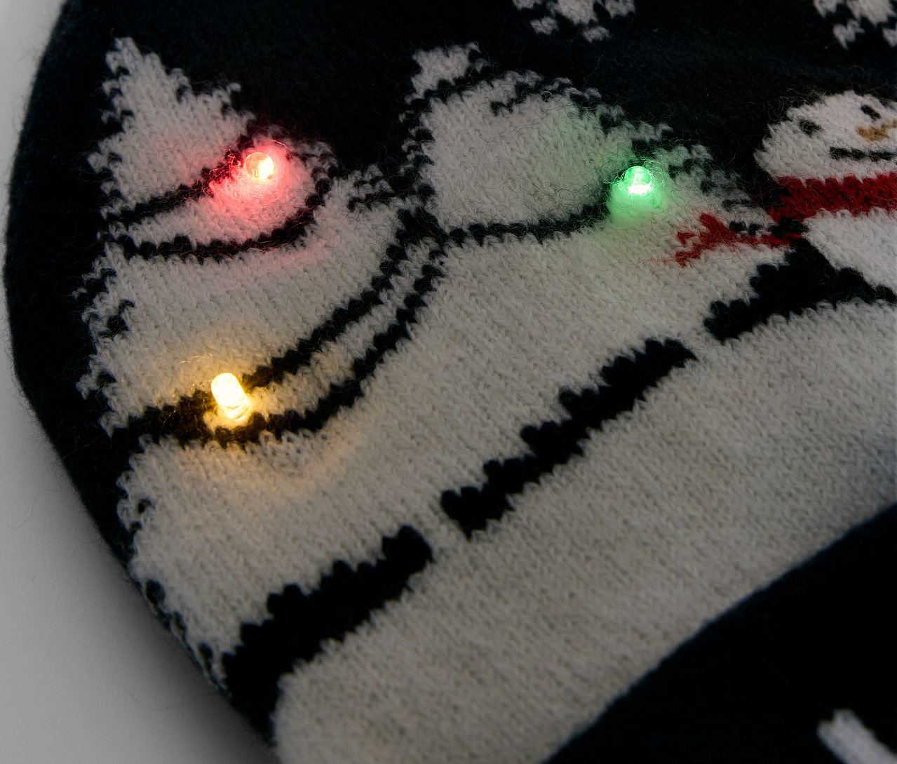 Kar taneleri ve kardan adamlarla süslenmiş, renkli ışıklarla bezenmiş siyah beyaz örgü bere detayı.