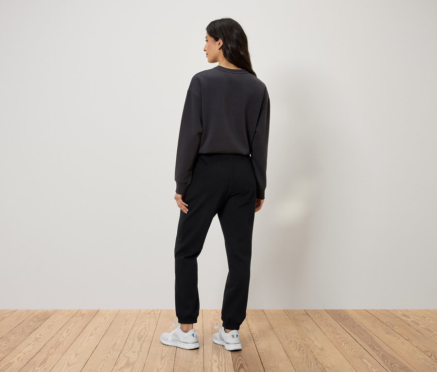 Siyah eşofman altı, gri sweatshirt ve beyaz ayakkabılar giyen bir kadının arkadan görünüşü.