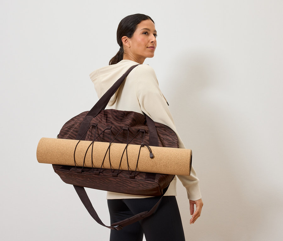 Kadın, üzerinde yoga matı olan kahverengi desenli bir spor çantası taşıyor