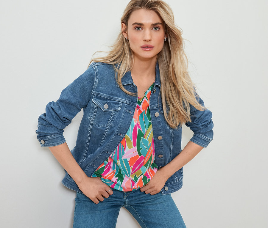 Kadın kot ceket, düşük omuzlu, baskılı tişört ve düz kesim kot pantolon ile poz veriyor.