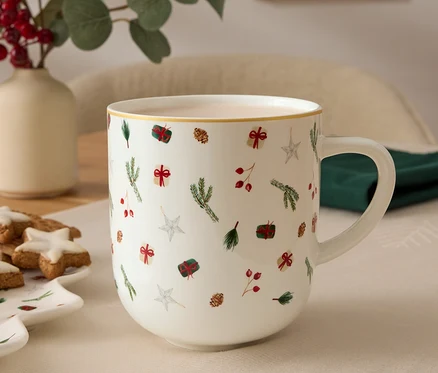 Ön planda Noel motifli bir kupa, arka planda bitkilerle dolu bir vazo ve kurabiye dolu bir tabak yer alıyor.