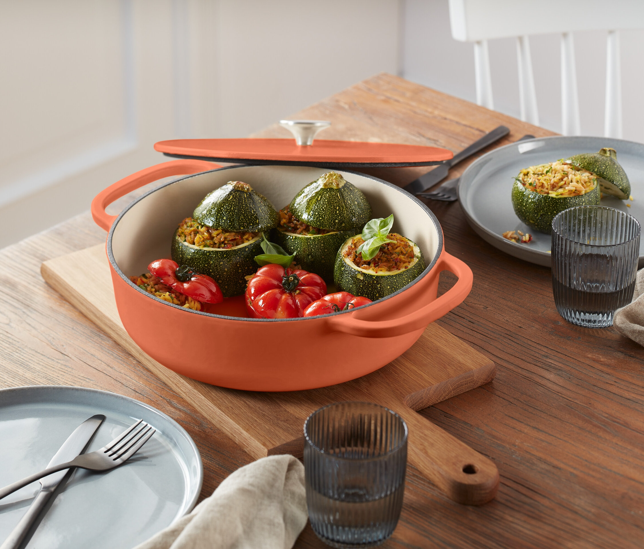 Ahşap kesme tahtası üzerinde turuncu bir tencerede dolmalık kabak ve domatesler.