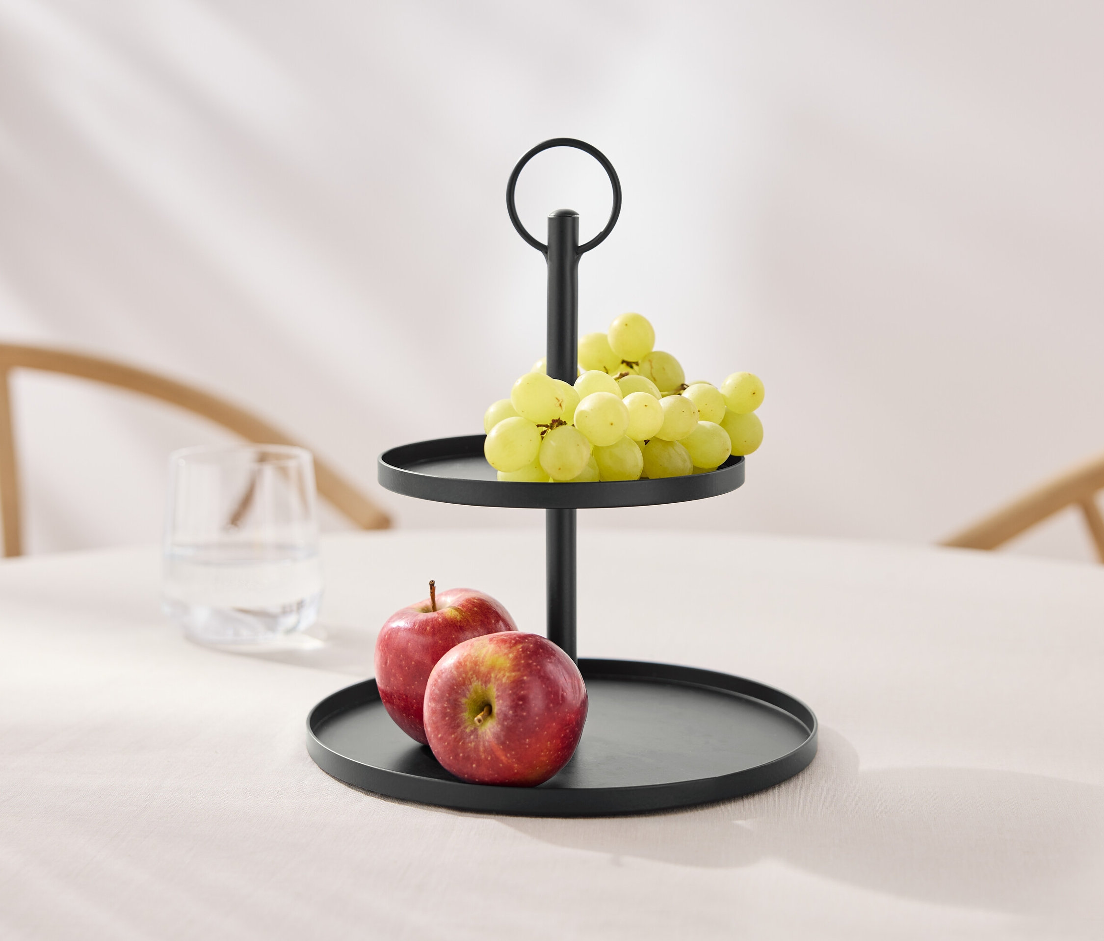 Masanın üzerinde üzüm ve elmalarla dolu iki katlı siyah bir sunumluk.