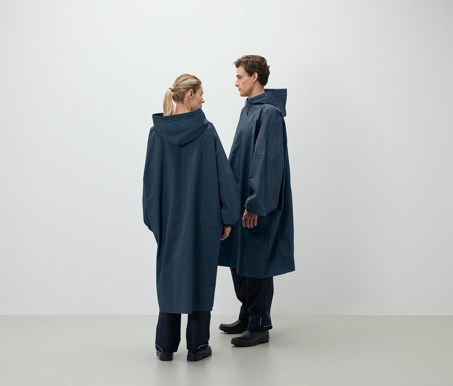 Bir erkek ve bir kadın karşı karşıya duruyor ve koyu mavi kapüşonlu yağmurluklar giyiyorlar.
