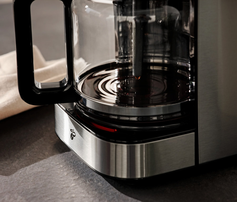 Arka planda bej rengi bir bezle kahve demliği olan bir kahve makinesinin yakın çekim görüntüsü.