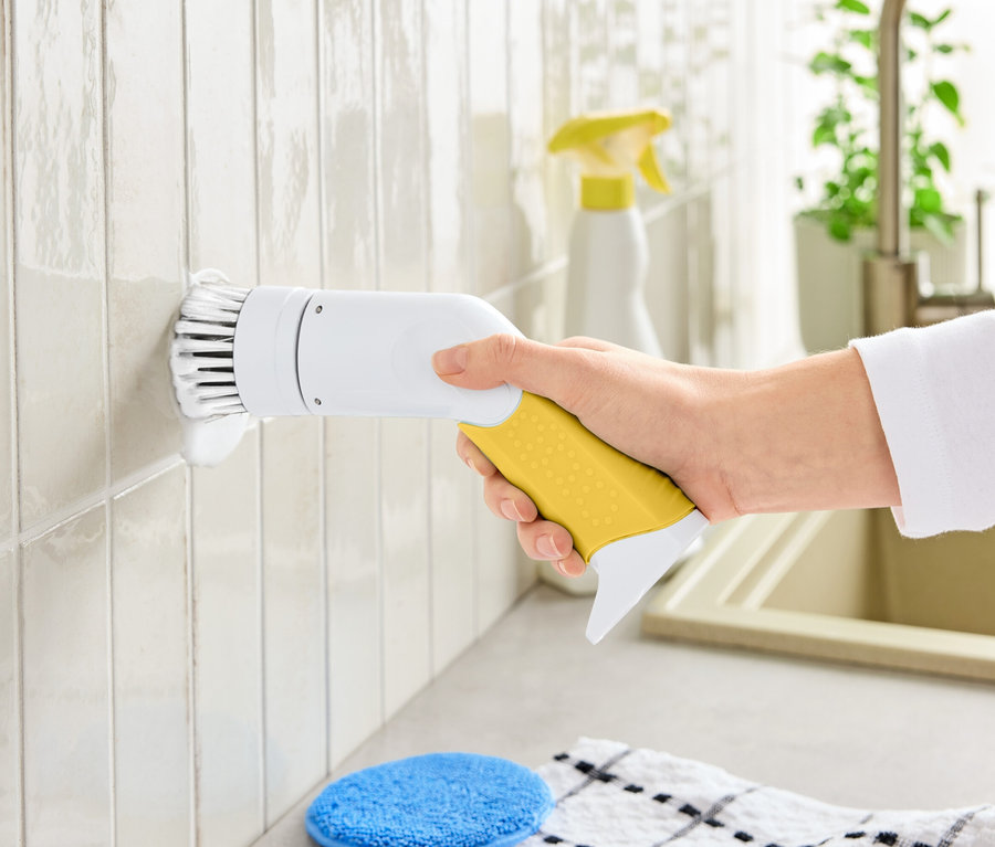 Bir el, fayansları temizlemek için sarı saplı ve beyaz başlıklı elektrikli bir temizleme fırçası tutuyor.