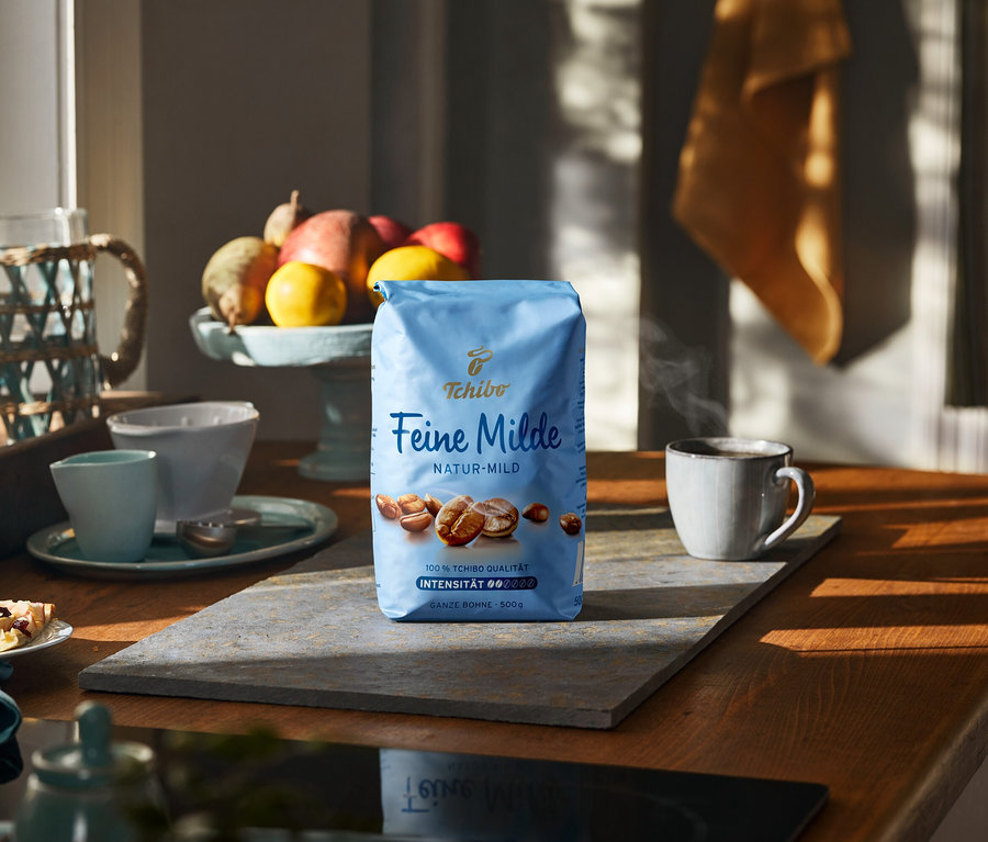 Taş bir yüzeyde bir fincan ve meyvelerin yanında 500g'lık bir paket Feine Milde kahvesi.