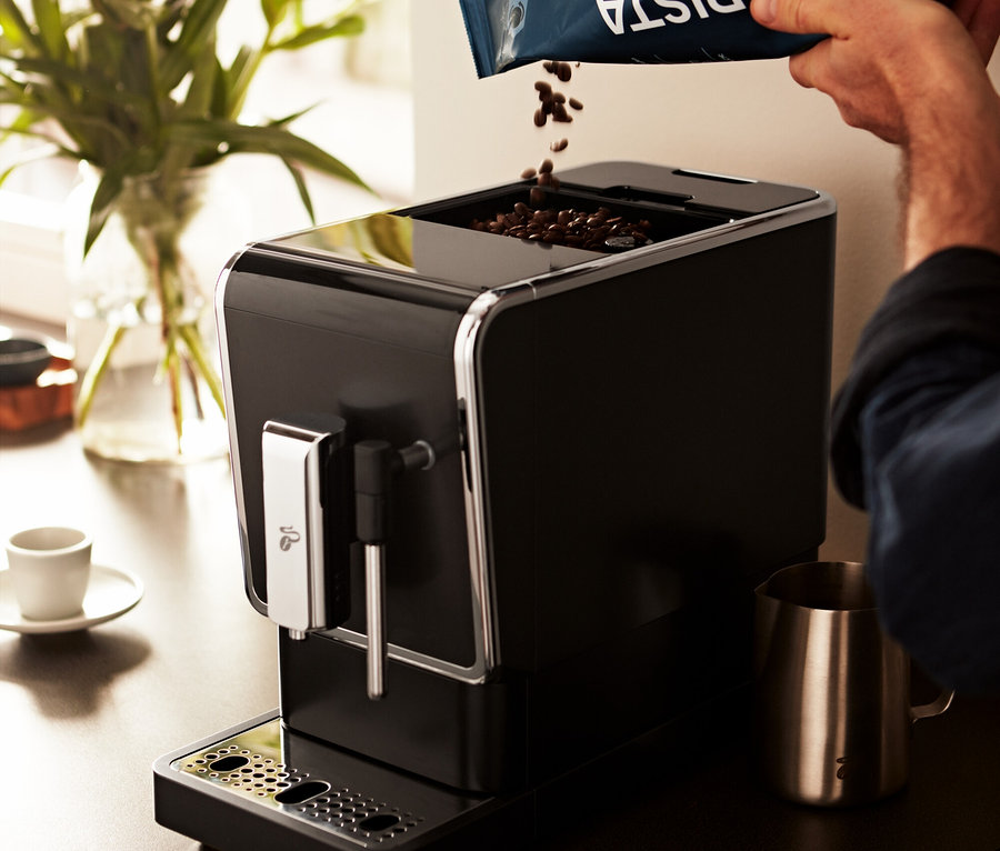 Adam »Esperto Latte« Antrasit Tchibo Tam Otomatik Kahve Makinesine kahve çekirdekleri döküyor.