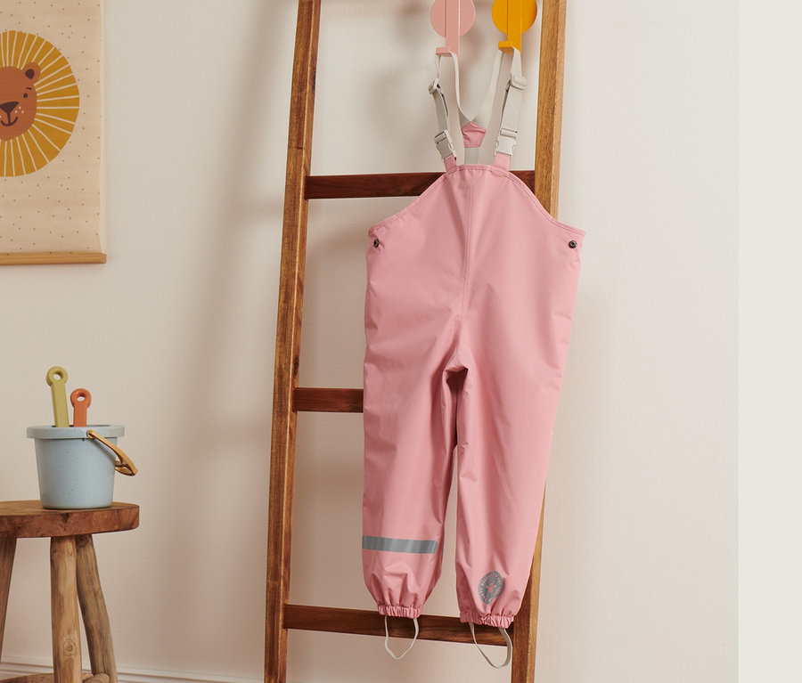 Pembe termal yağmur pantolonu ahşap bir merdivene asılı duruyor.