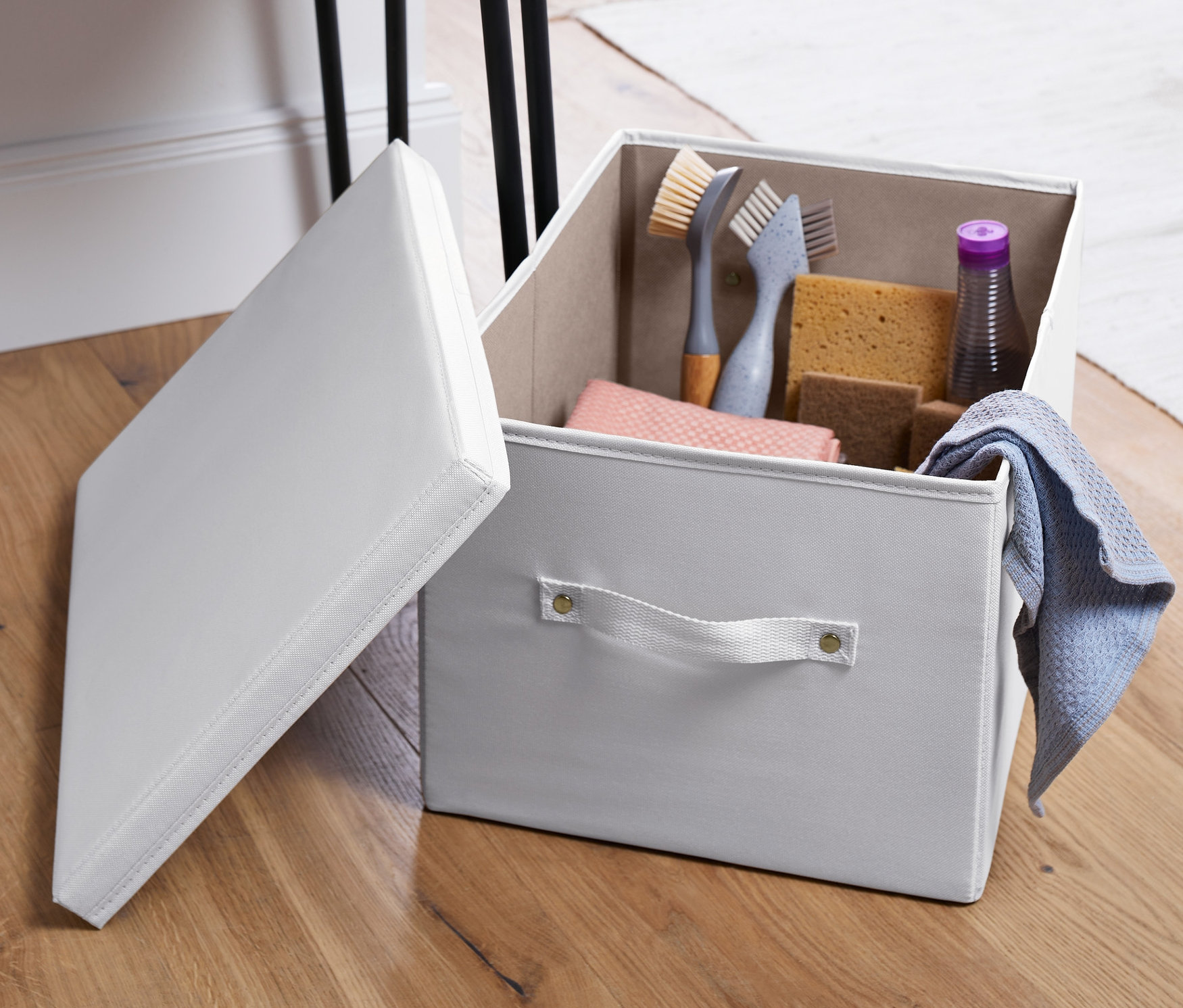 Ahşap zeminde, masanın yanında açık gri kapaklı düzenleme sandığı.