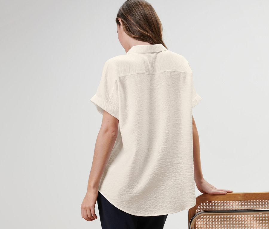 Kadın arkası dönük duruyor, bir bluz giyiyor ve bir sandalyeye yaslanıyor.