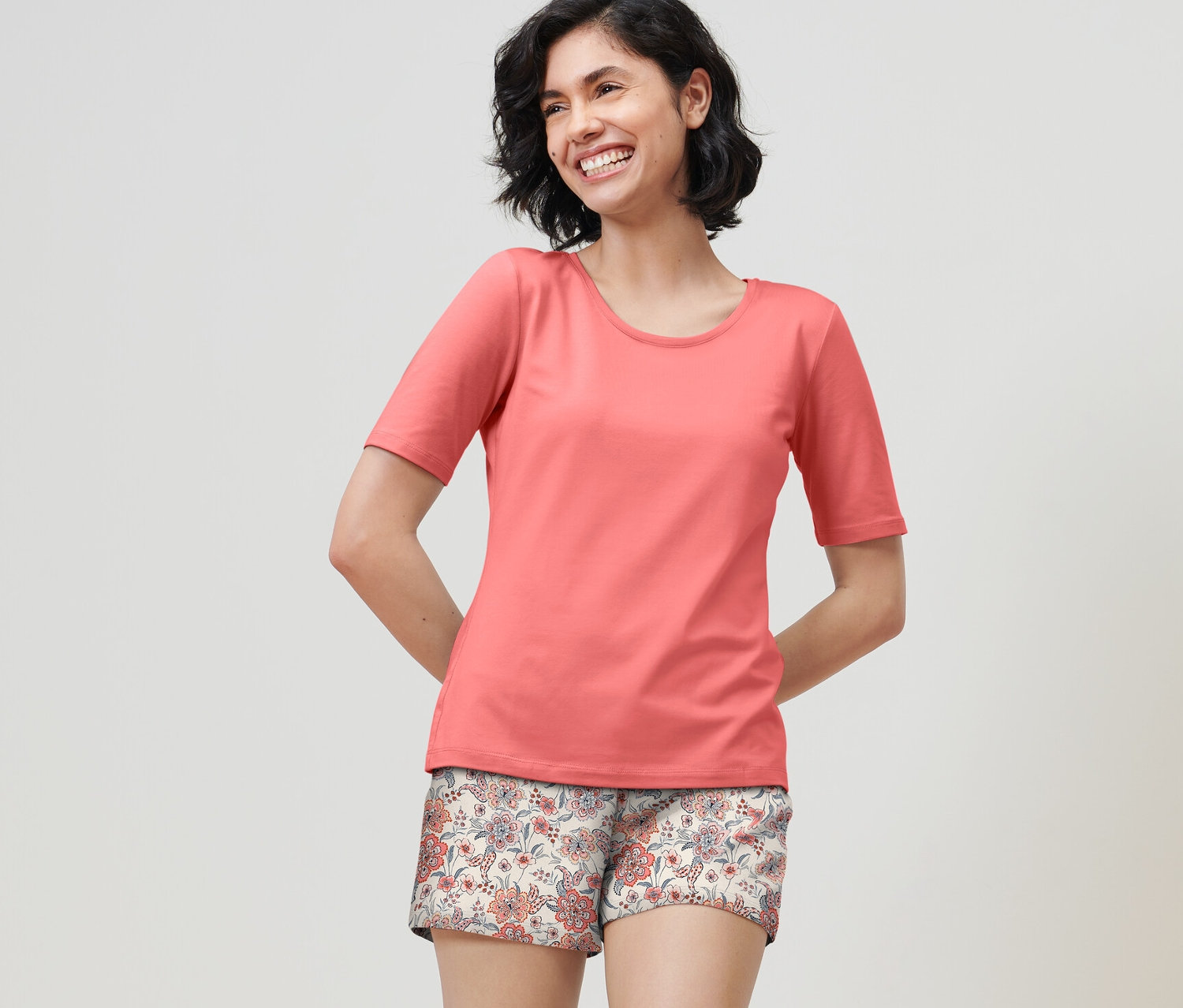 Gülümseyen bir kadın papaya rengi şortlu pijama takımı giyiyor.