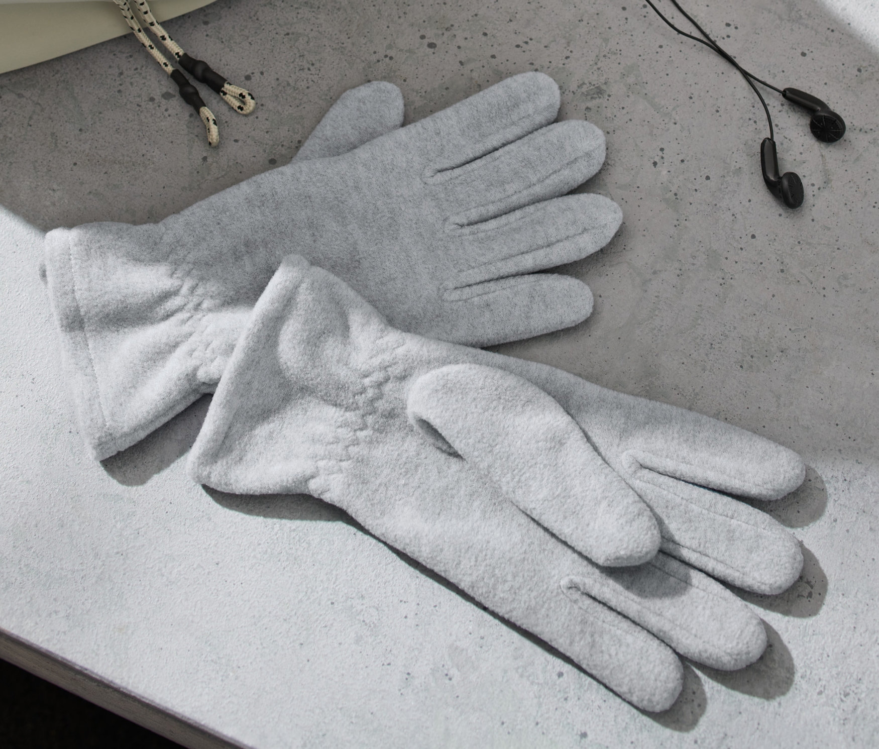 Gri renkli iki polar eldiven, kulaklık ve bir çantanın yanında gri bir yüzeyde duruyor.