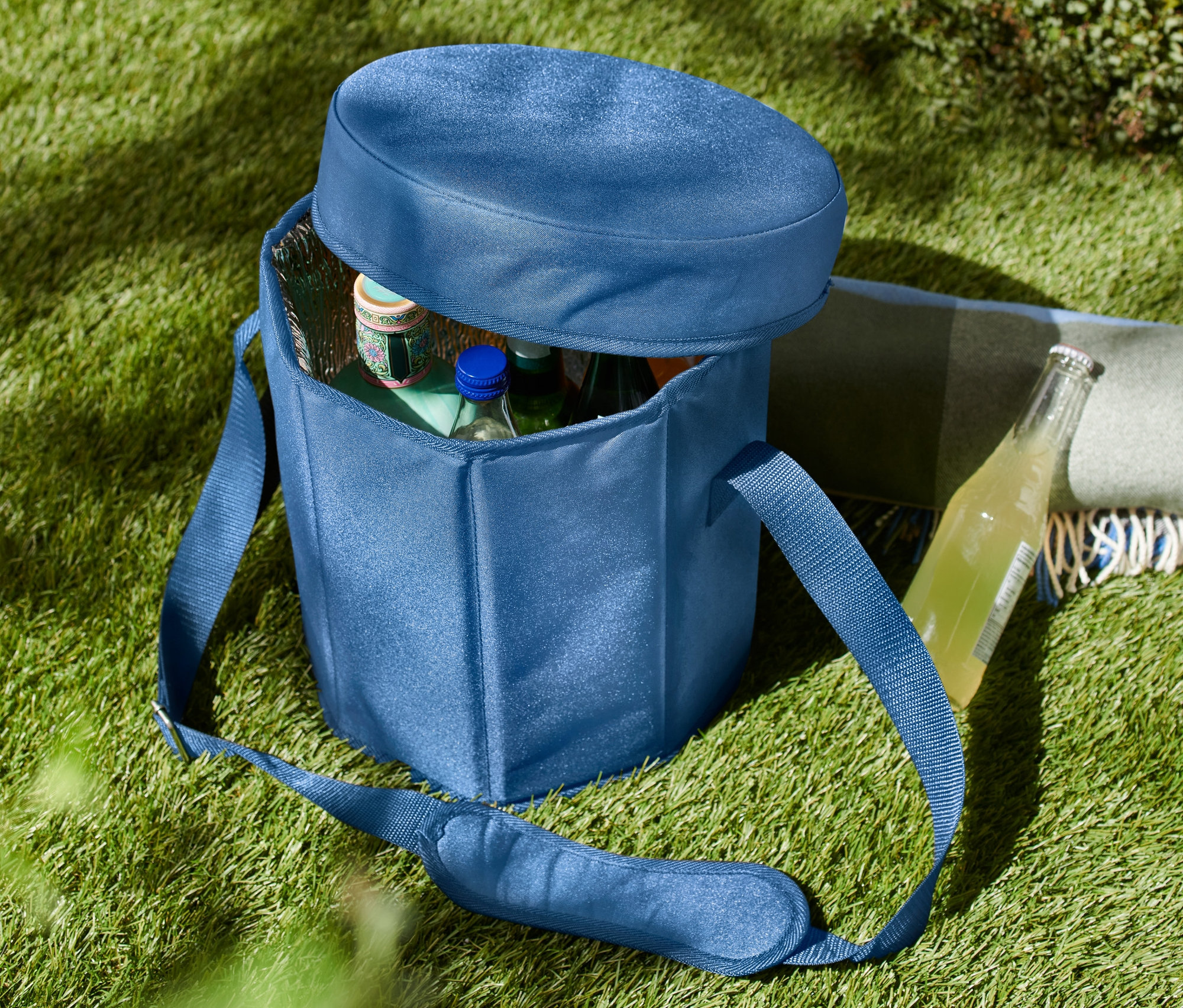 Çim üzerinde, kısmen açık, içinde şişeler bulunan mavi renkli 2'si 1 arada soğutucu çanta.