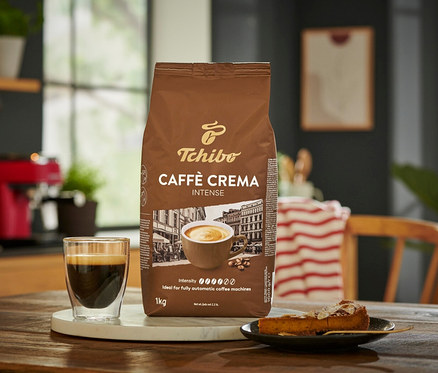 Bir fincan kahve ve bir dilim kekin yanında bir paket Caffè Crema Intense – 1 kg kahve çekirdeği.