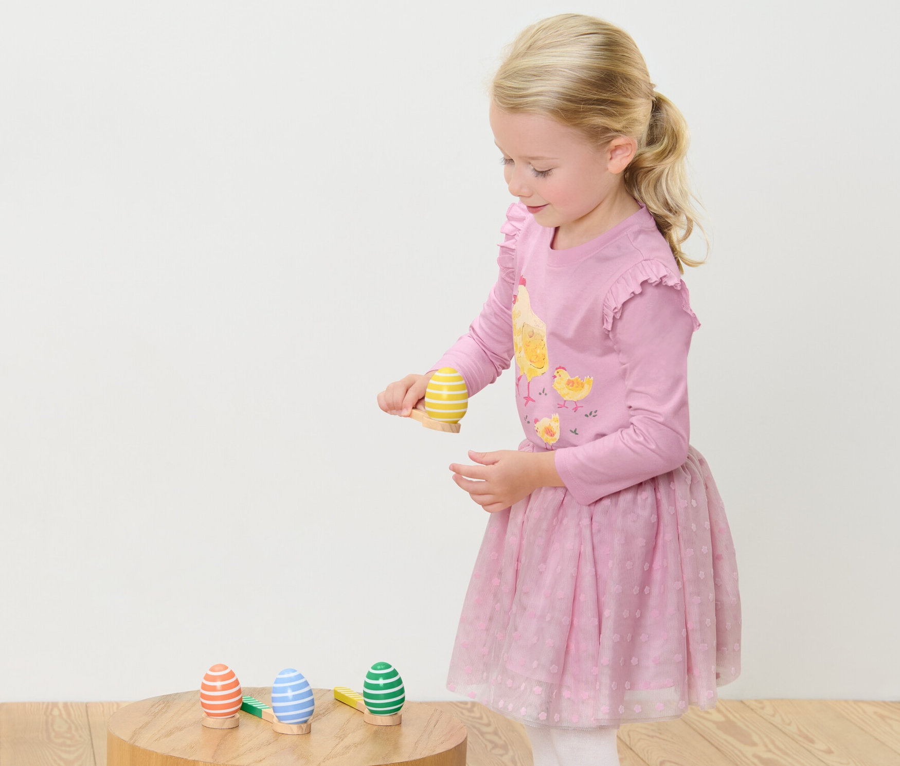 Kız çocuğu Yumurta Yarışı Oyunu oynuyor. Ayakta duruyor ve bir yumurtayı kaşıkta dengelemeye odaklanıyor.