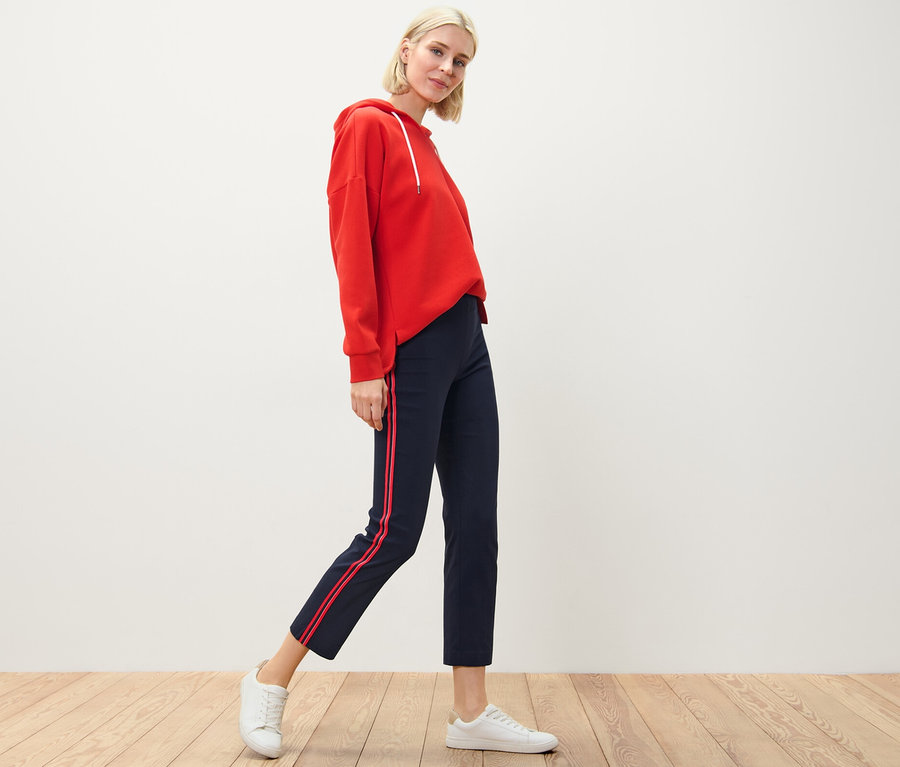 Sarışın bir kadın, kırmızı kapüşonlu ve şeritli streç pantolonla poz veriyor.