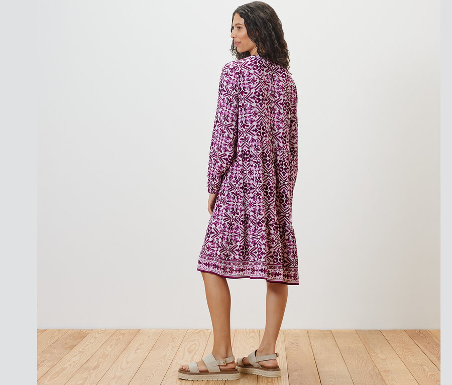 Kadın baskılı dokuma elbise giyerek arkadan poz veriyor.