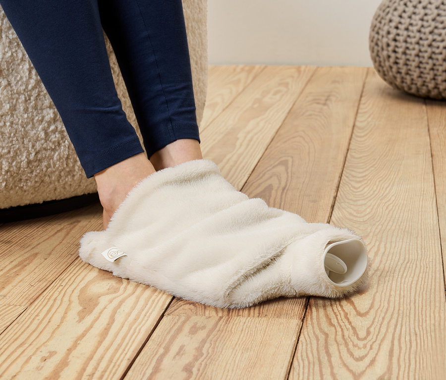 Mavi taytlı ayaklar, kabarık, krem rengi bir sıcak su torbası kılıfının içine sokulmuş.