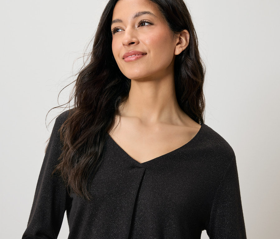 Siyah, parıltılı, V yakalı bir üst giyen, uzun, koyu renkli saçlı, gülümseyen bir kadının portresi.