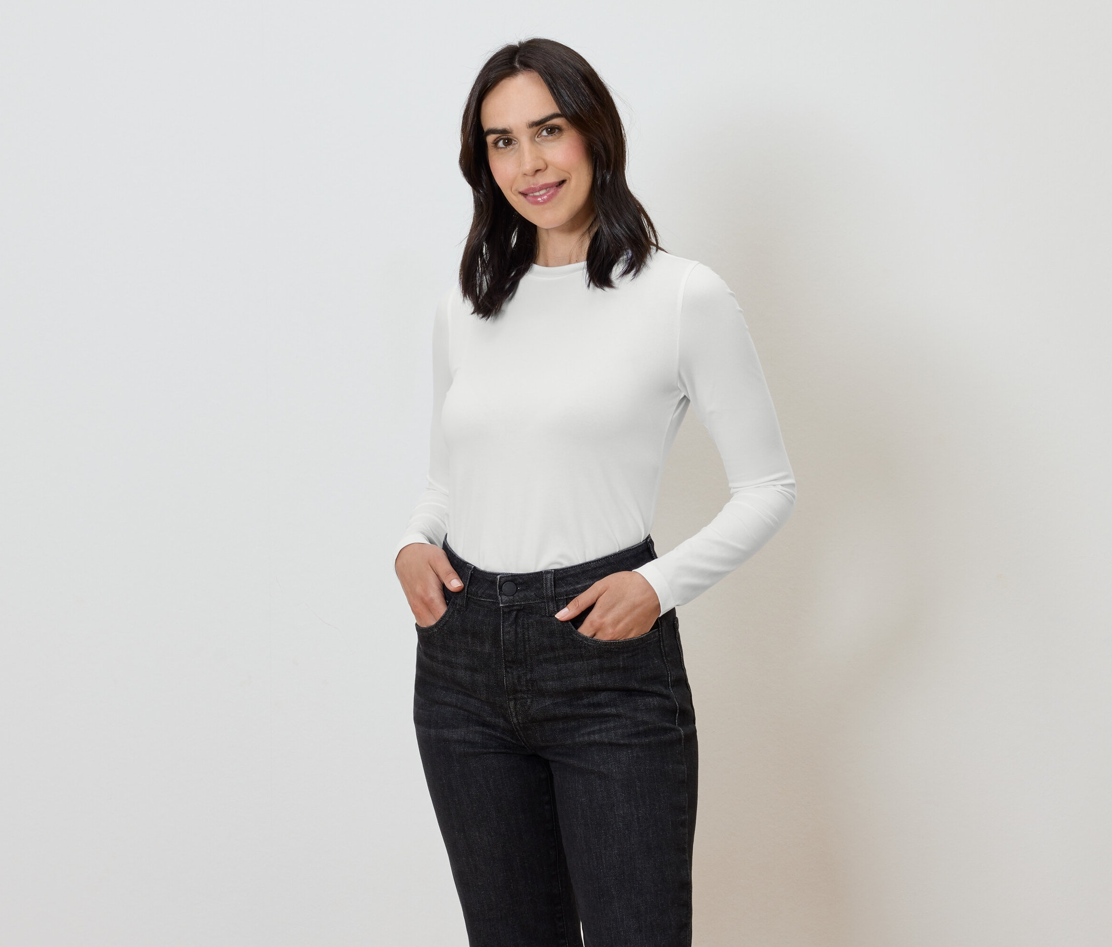 Elleri koyu renk kot pantolonunun cebinde, üzerinde beyaz uzun kollu tişört olan bir kadın.