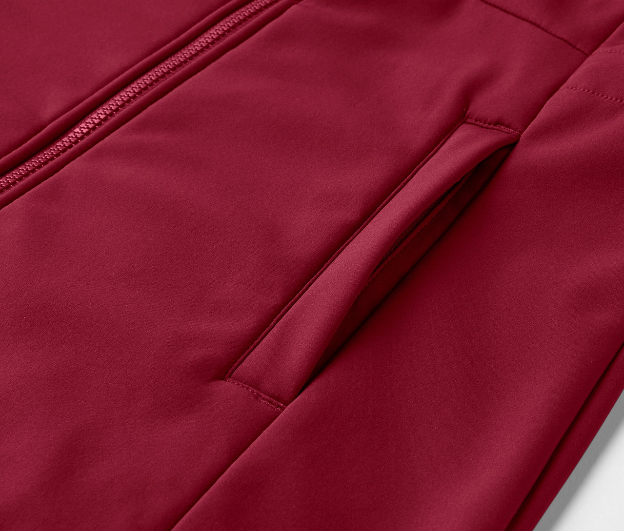 Koyu kırmızı softshell montun fermuar ve cep detayının yakın çekimi.