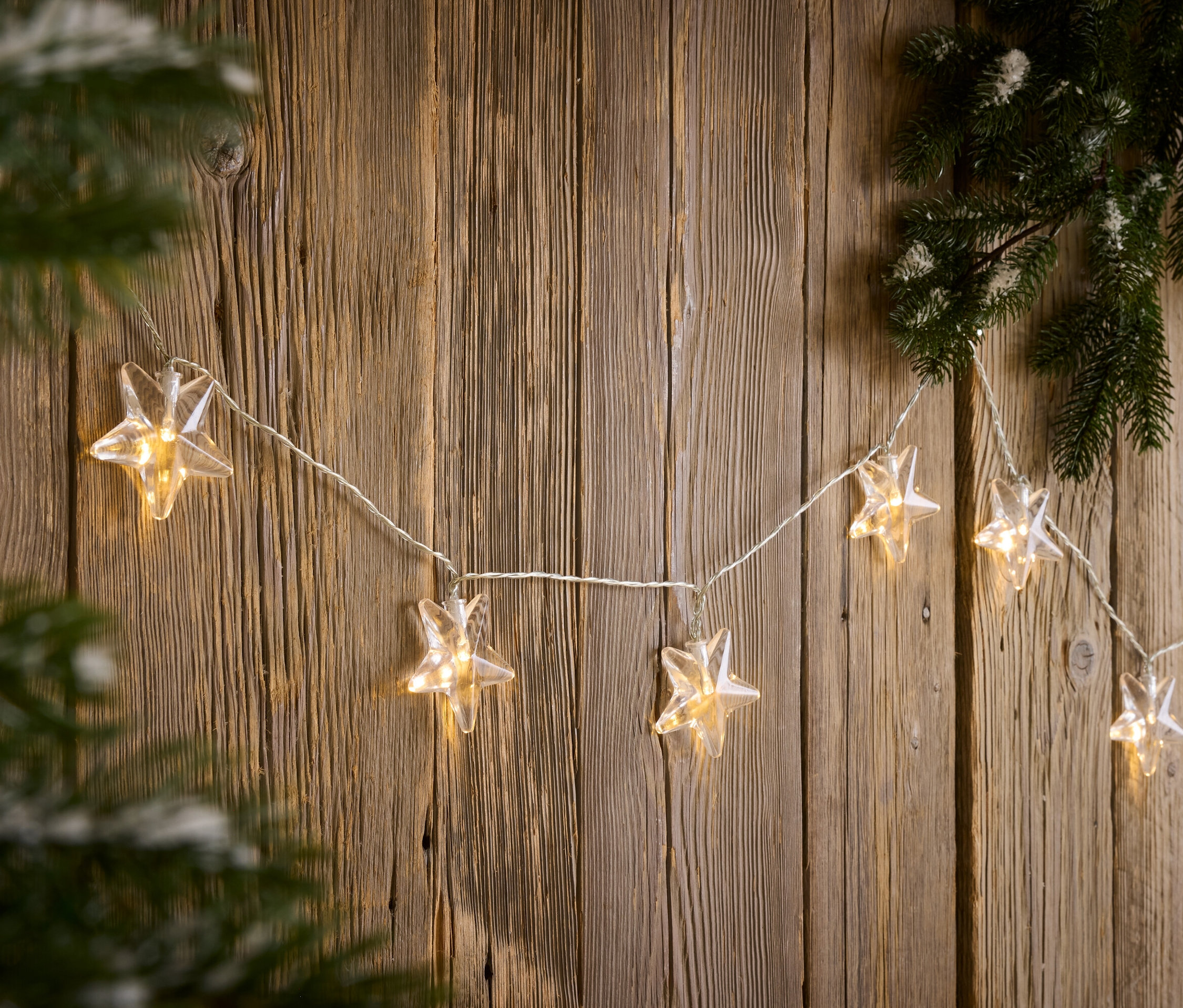 Yıldız şeklinde bir ışık zinciri, çam dalının yanındaki ahşap bir duvara asılıdır.