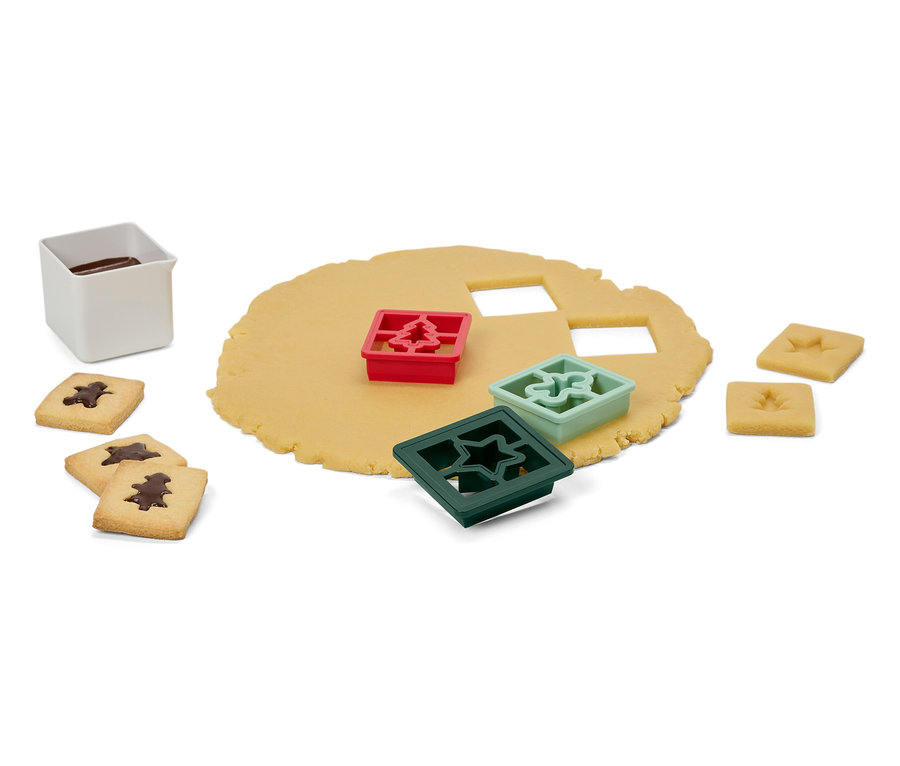 Ağaç, yıldız ve süs şeklinde kalıpları olan hamur, bitmiş kurabiyeler ve sır içeren beyaz bir kap.