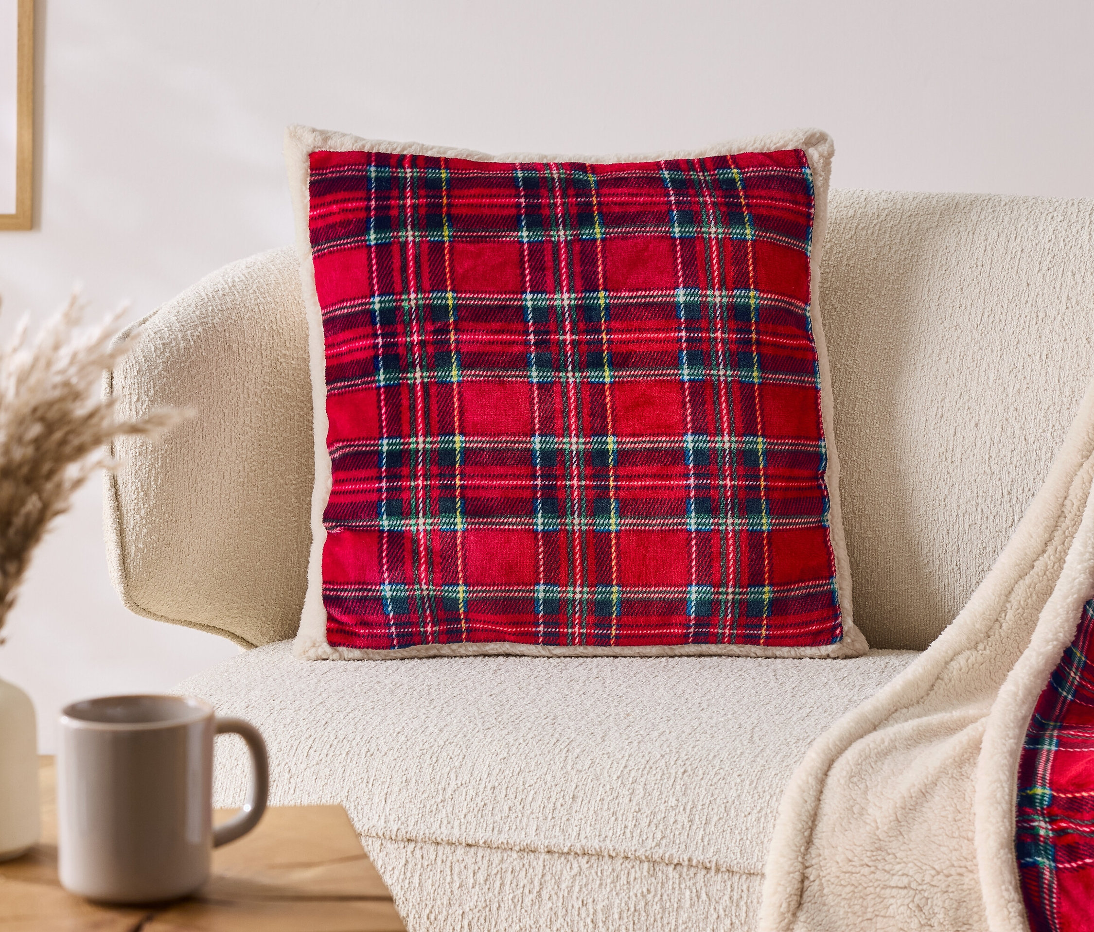 Kırmızı ekose yastık, bej renkli bir kanepede ekose bir battaniyenin yanında duruyor.