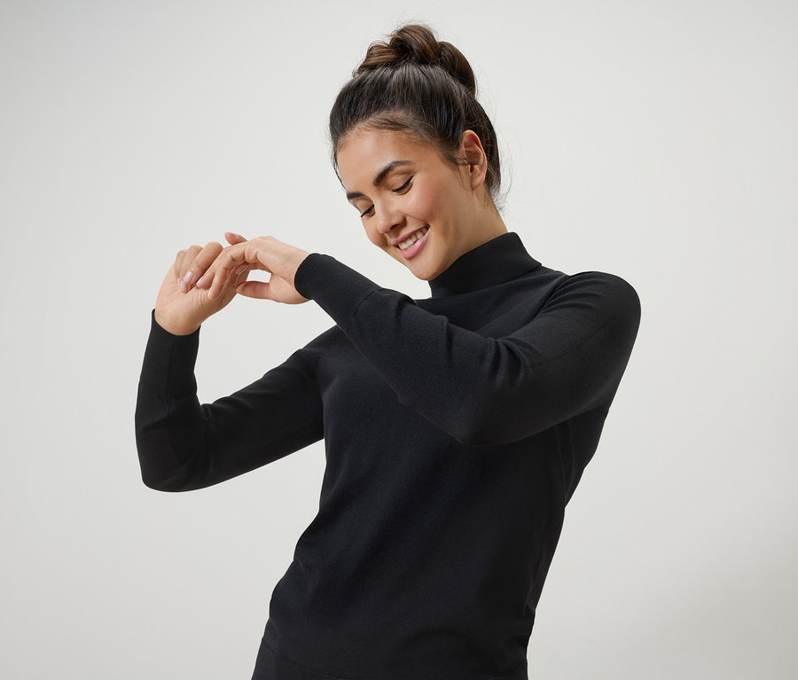 Kadın siyah balıkçı yaka kazakla gülümsüyor ve poz veriyor.