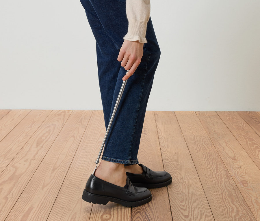 Bir kişi ayakkabı çekeceği kullanarak siyah loafer ayakkabı giyiyor.