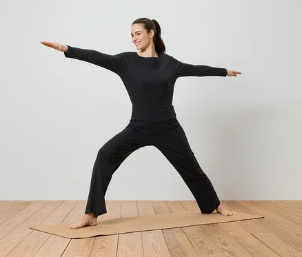 Siyah spor giyim kıyafetleri içinde bir kadın, yoga matı üzerinde yoga yapıyor.