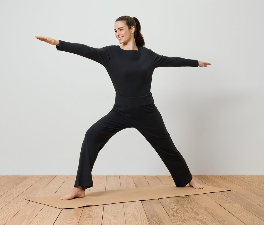 Siyah spor giyim kıyafetleri içinde bir kadın, yoga matı üzerinde yoga yapıyor.