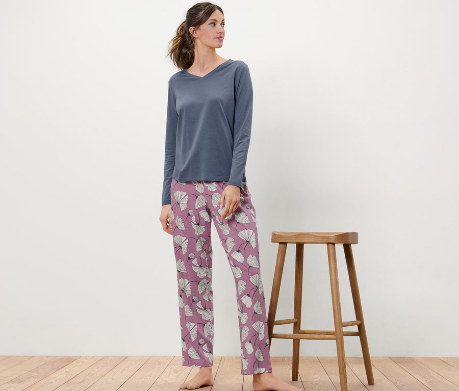 Kadın ahşap bir taburenin yanında duruyor, üzerinde çiçek desenli bir pijama var.