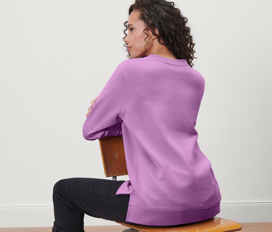 Kadın sandalyede oturuyor ve sweatshirt giyiyor.