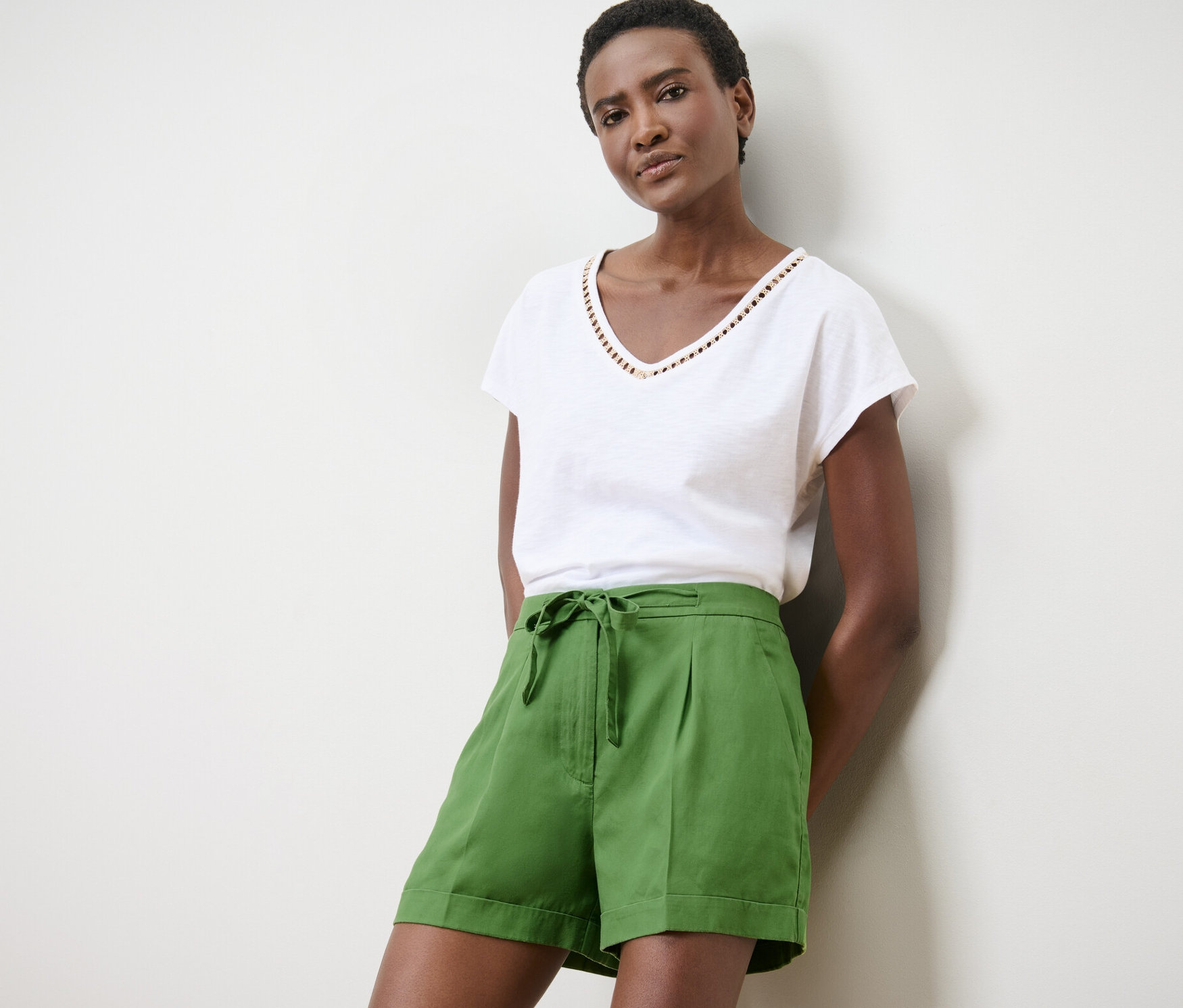 Kadın yeşil keten şort ve beyaz tişörtle poz veriyor.