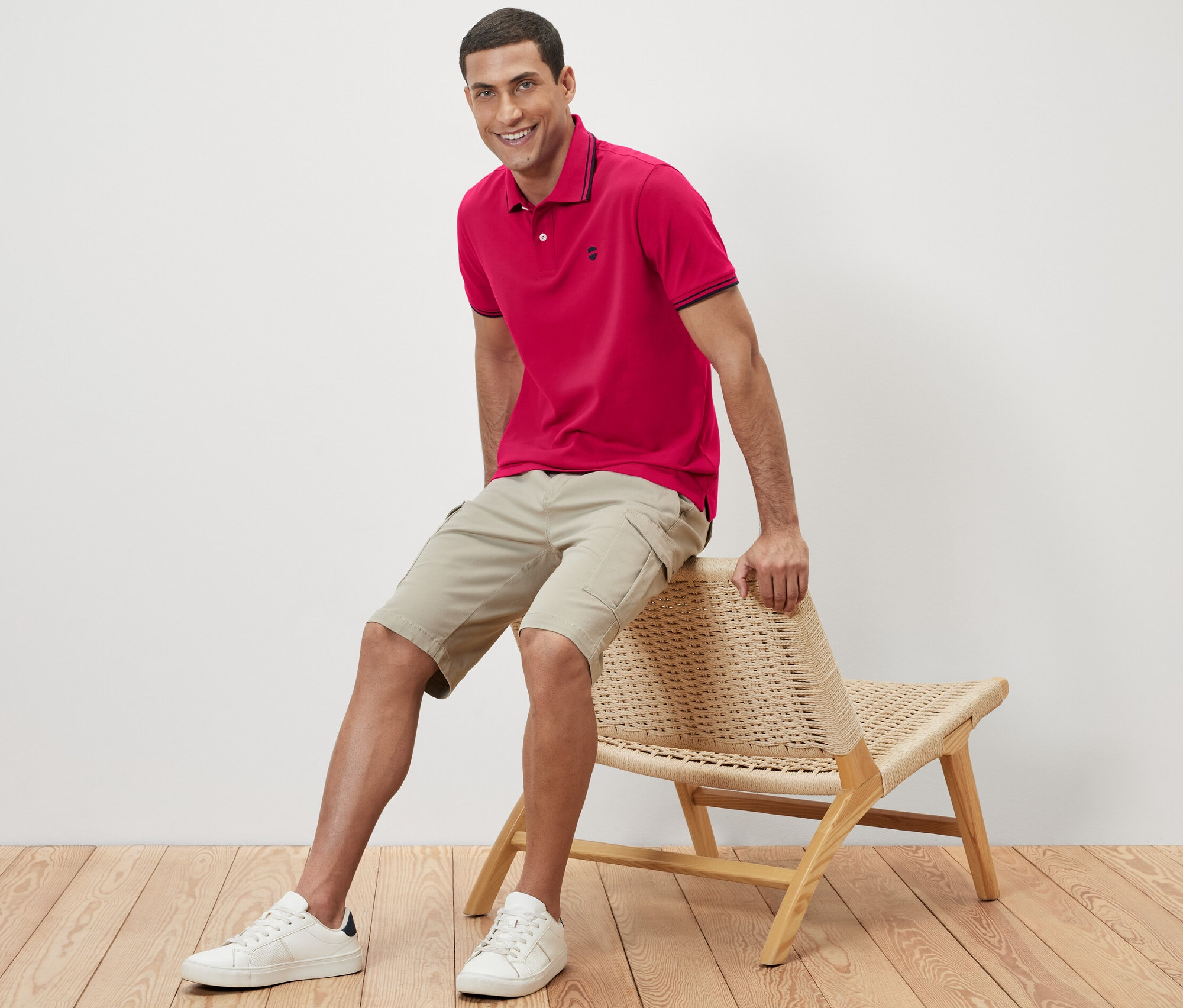 Adam hasır bir sandalyede oturuyor ve pembe bir pike polo yaka tişört giyiyor.