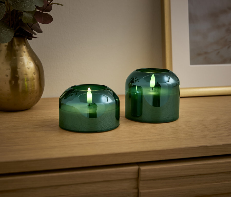 Ahşap bir masa üzerinde iki adet yeşil mum ve altın bir vazo bulunmaktadır.