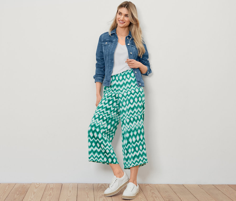 Sarışın bir kadın kot ceket, beyaz dokulu tişört ve baskılı saten pantolonla poz veriyor.