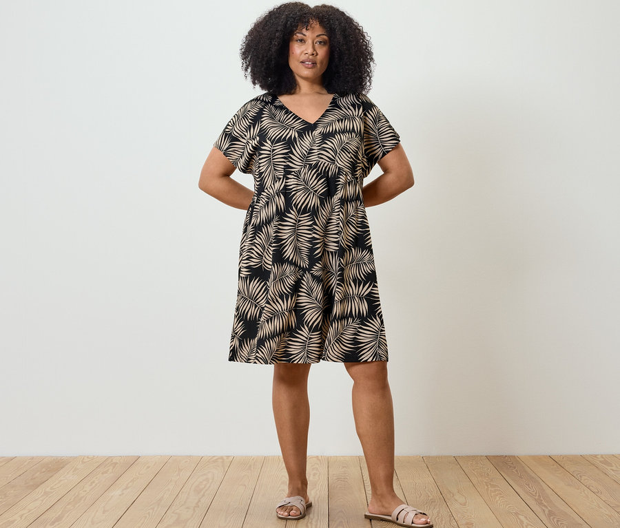 Bir kadın elleri arkasında duruyor ve baskılı bir jarse elbise giyiyor.