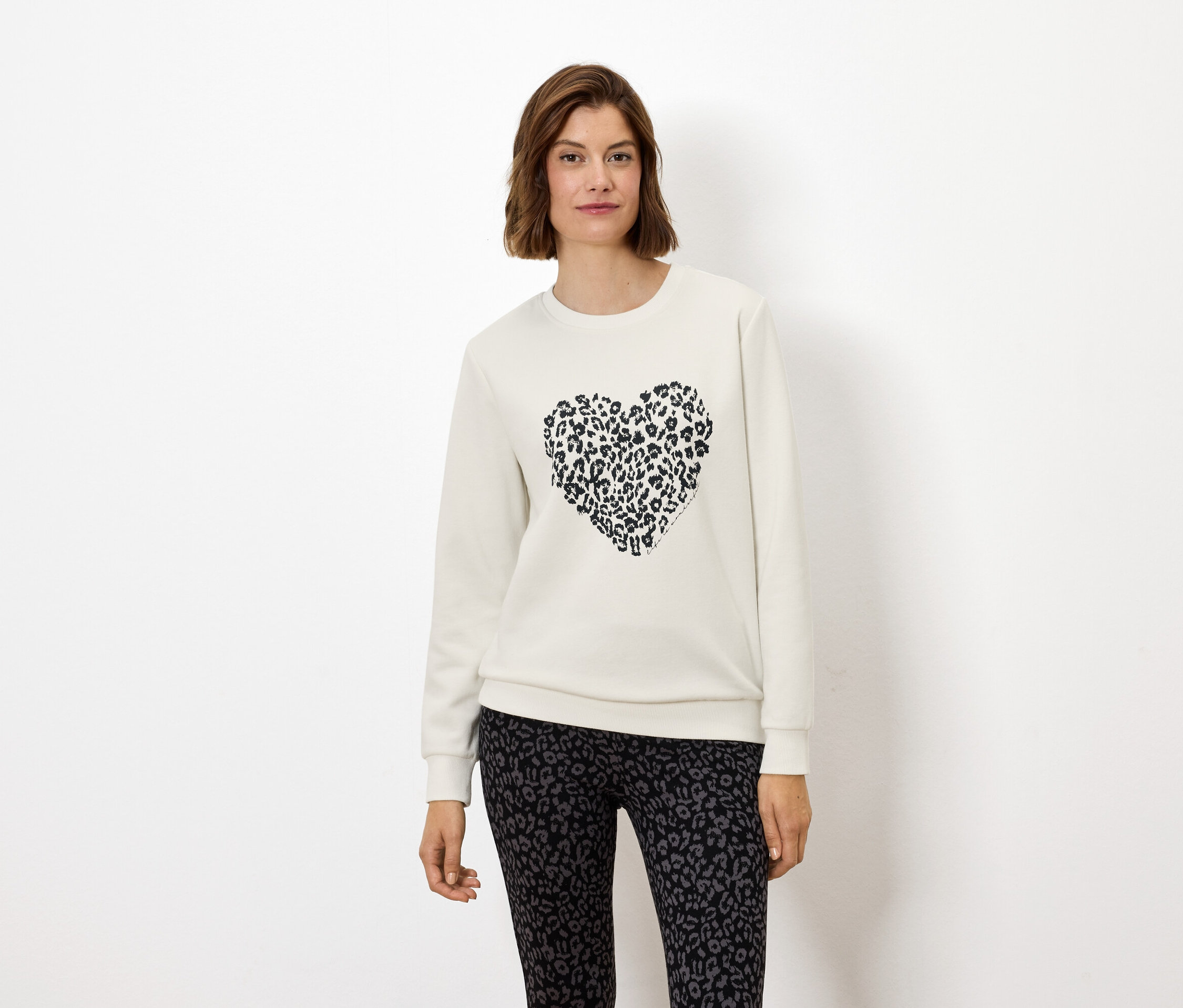 Kadın, hayvan baskılı bir kalbe sahip beyaz bir sweatshirt ve hayvan baskılı tayt giyiyor.