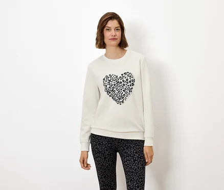 Kadın, hayvan baskılı bir kalbe sahip beyaz bir sweatshirt ve hayvan baskılı tayt giyiyor.
