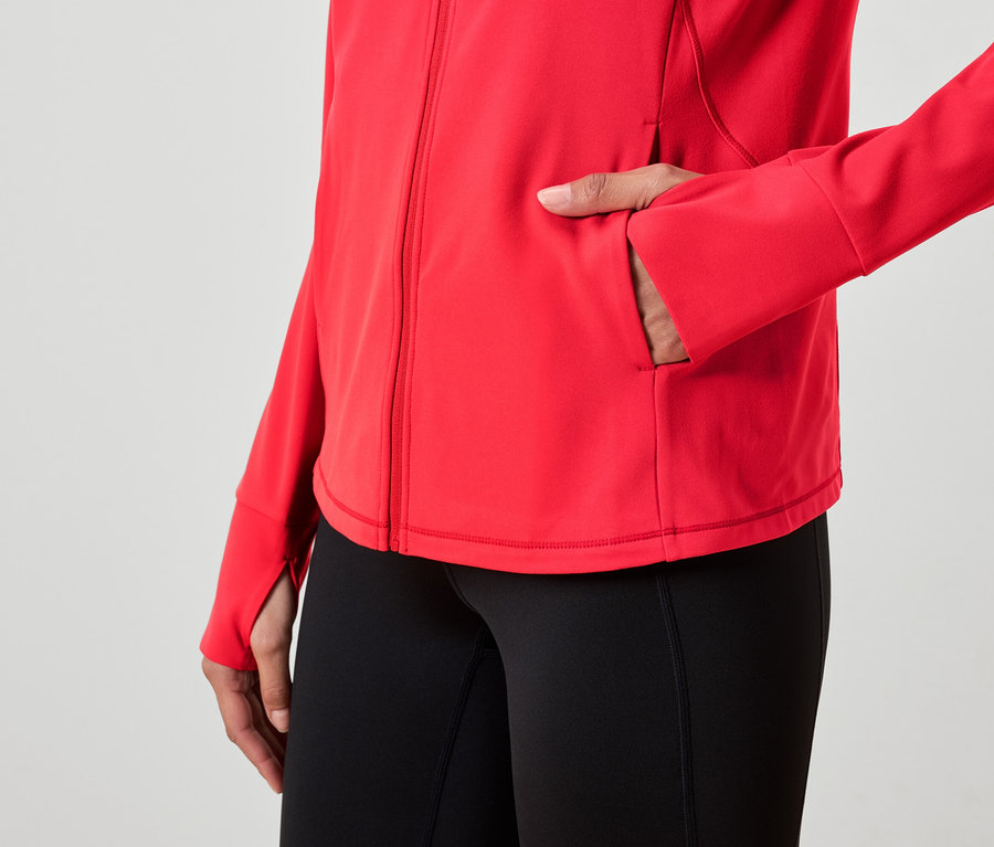 Kadın kırmızı bir ceketin cebine elini sokmuş ve siyah tayt giyiyor.