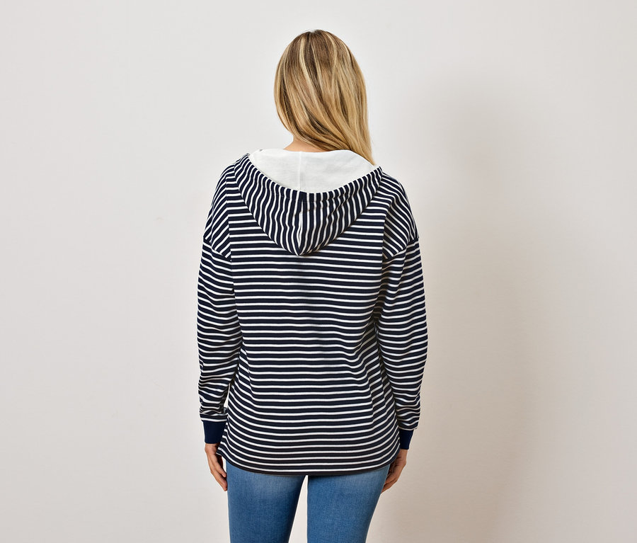 Arkadan, mavi beyaz çizgili kapüşonlu sweatshirt ve kot pantolon giyen sarışın bir kadın görülüyor.