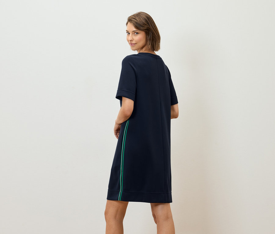 Kadın omzunun üzerinden bakıyor ve üzerinde yeşil şeritli lacivert bir tişört elbise var.