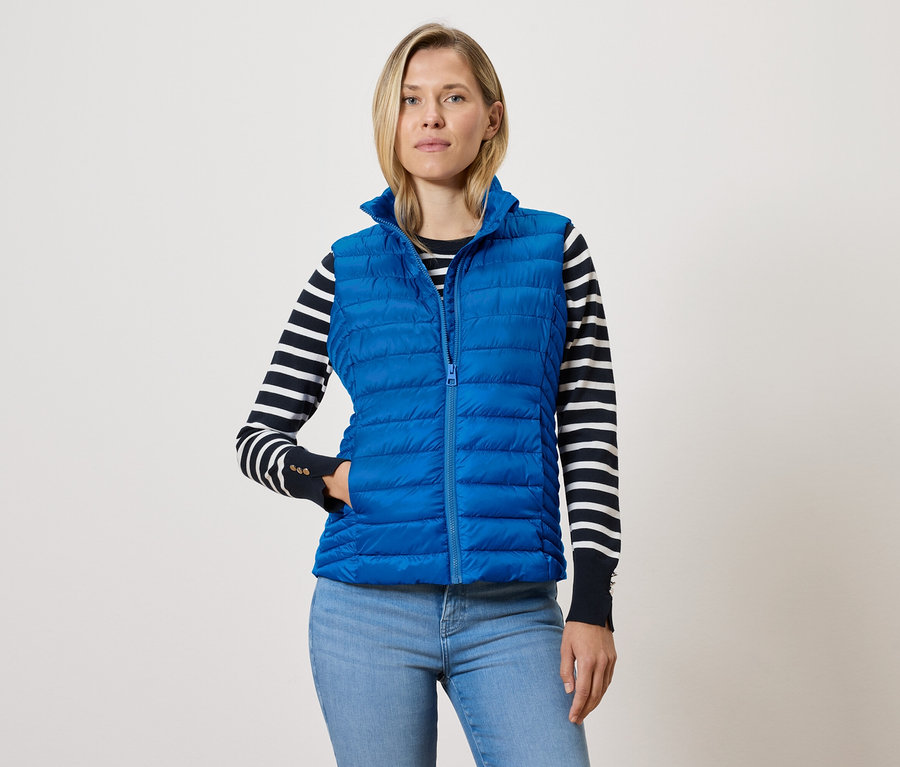 Mavi fermuarlı kapitone yelek, siyah beyaz çizgili kazak ve mavi kot pantolon giyen kadın.