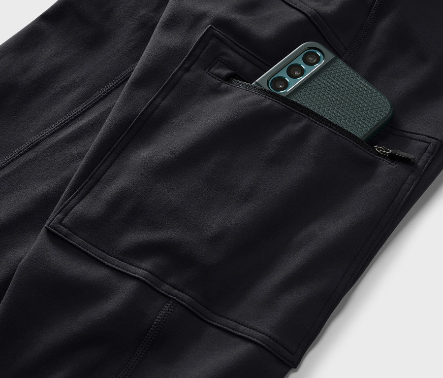 Cebinde yeşil cep telefonu olan siyah outdoor taytının yakın çekimi.